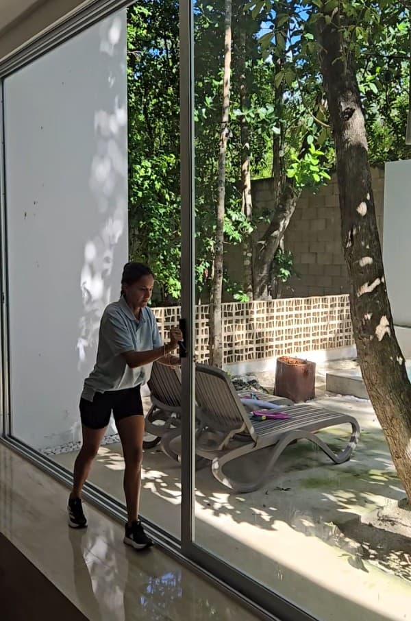 Qtana cleaner wiping the glass patio door of a rental unit with a garden view
